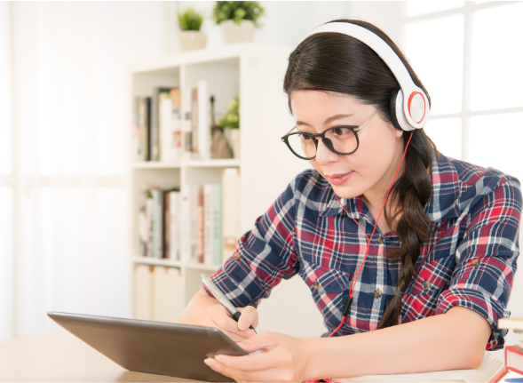 Une étudiante travaille sur sa tablette, casque sur les oreilles